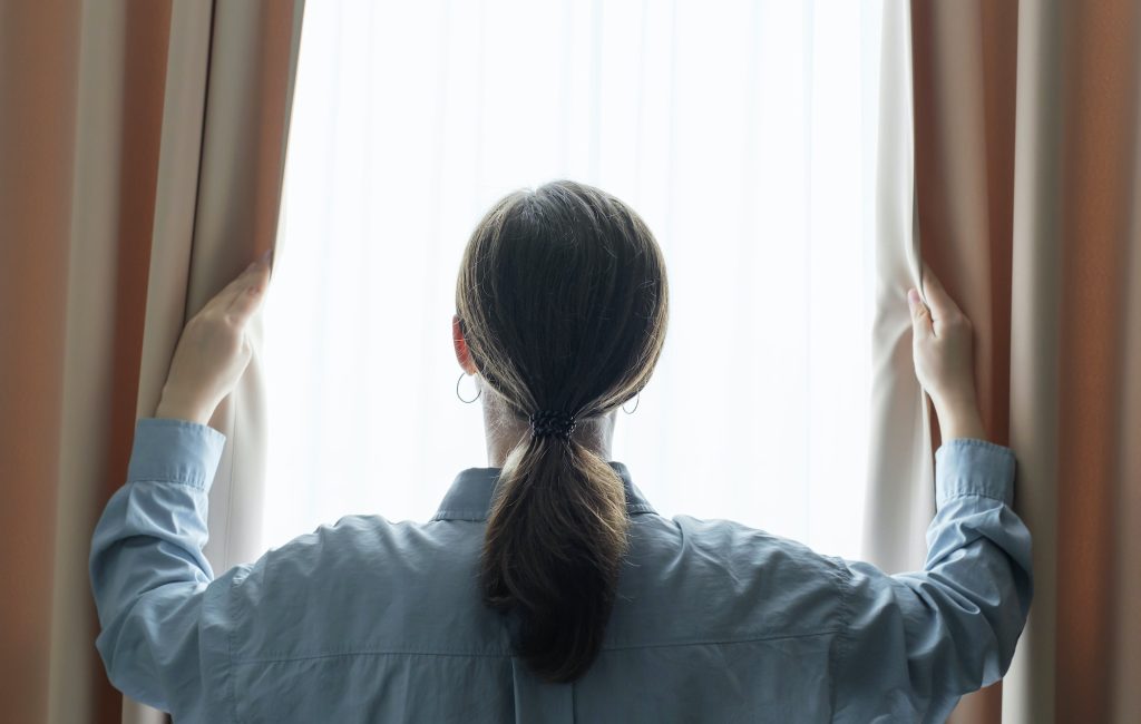 young-woman-stands-at-window-and-opens-curtains-back-view-.jpg